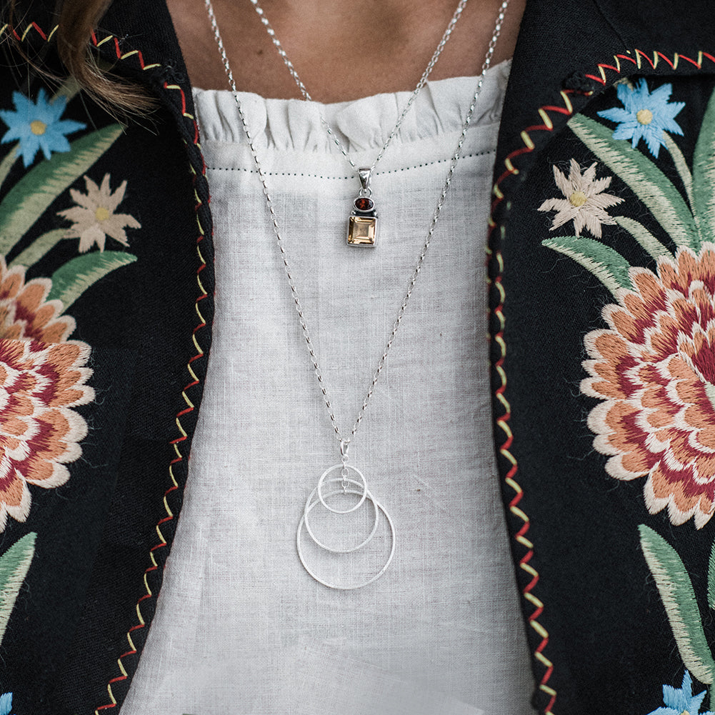 Close-up of model wearing silver three hoop necklace and a embroidered jacket