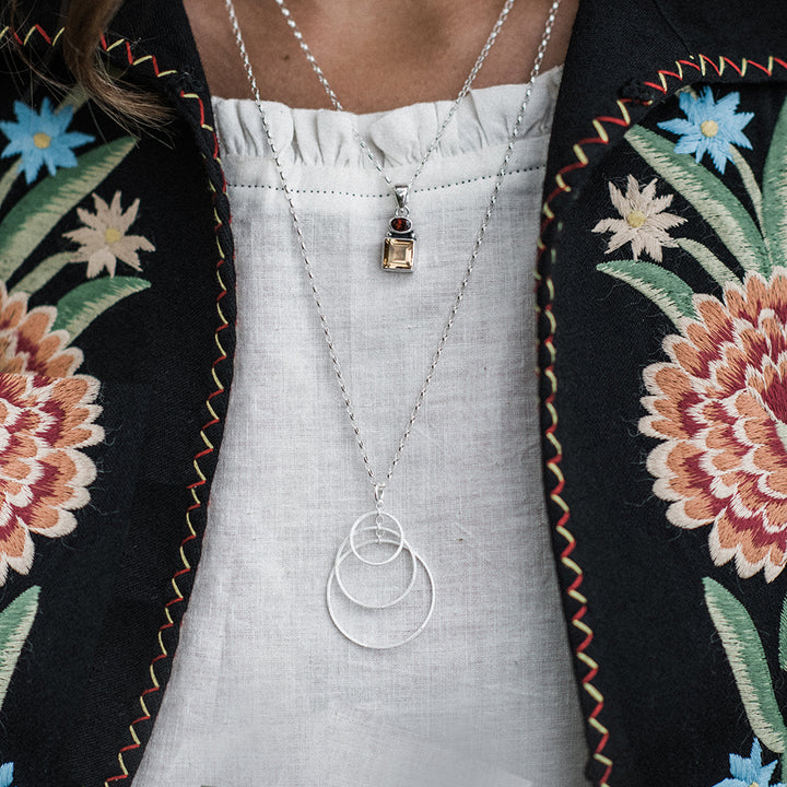 Close-up of model wearing silver three hoop necklace and a embroidered jacket