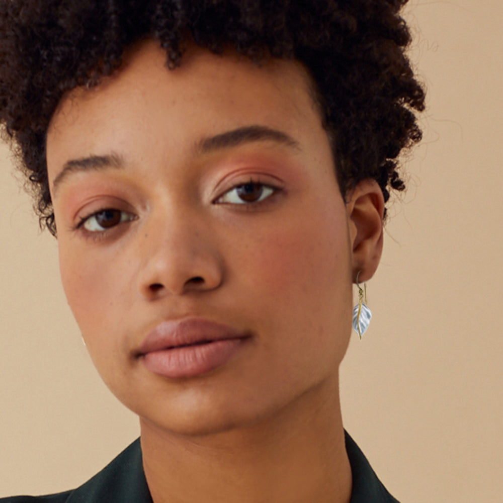 Close-up of a model with silver and gold leaf earrings against a cream background