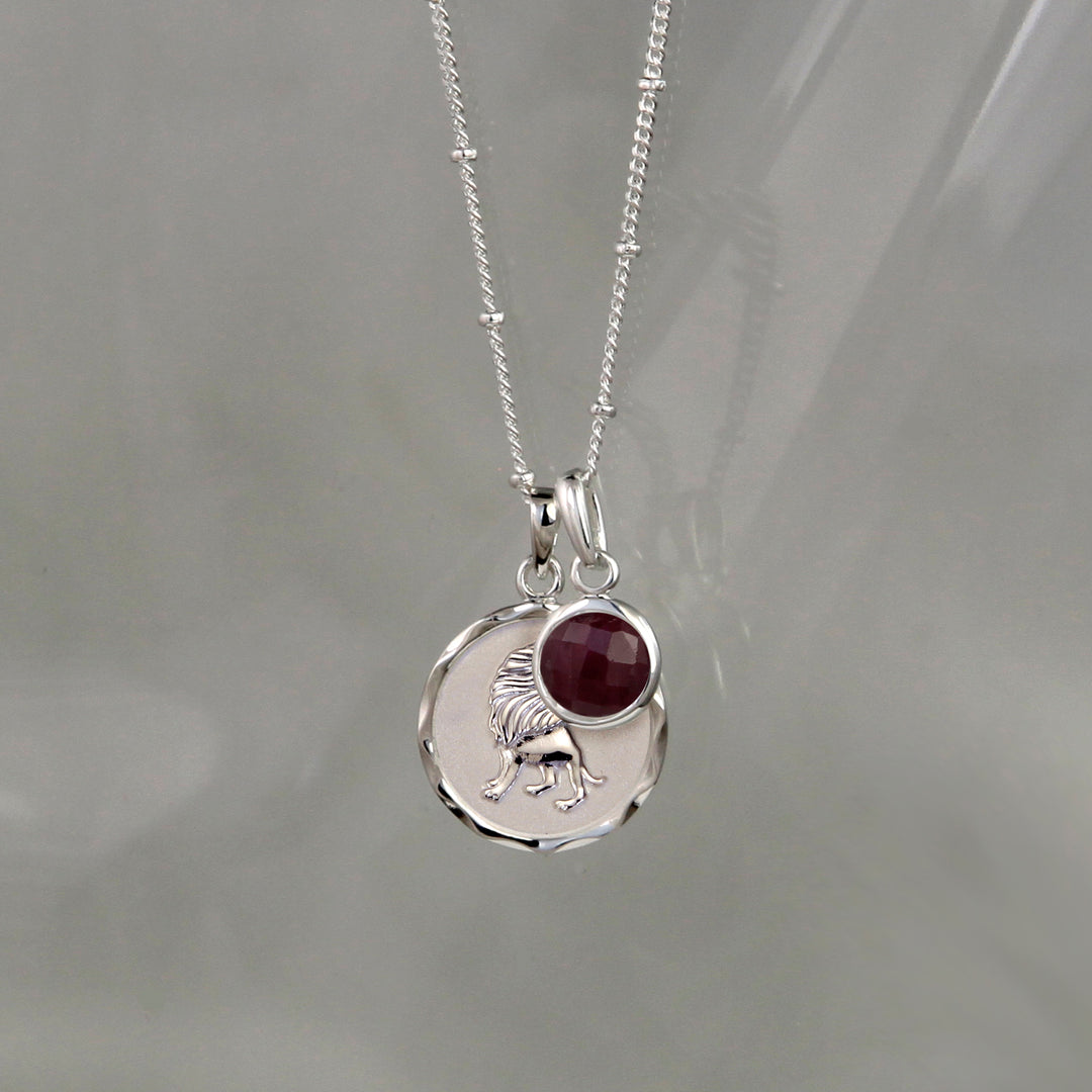 Silver Leo zodiac pendant and ruby July birthstone charm on gray background