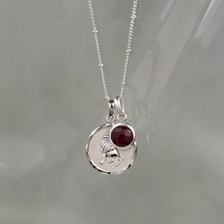Silver Leo zodiac pendant and ruby July birthstone charm on gray background