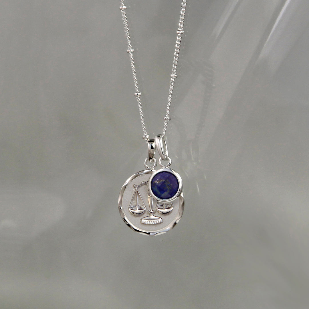 Silver Libra zodiac necklace and lapis lazuli September birthstone charm on a gray background