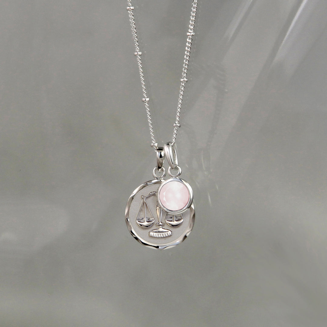 Silver Libra zodiac necklace and rose quartz October birthstone charm on a gray background