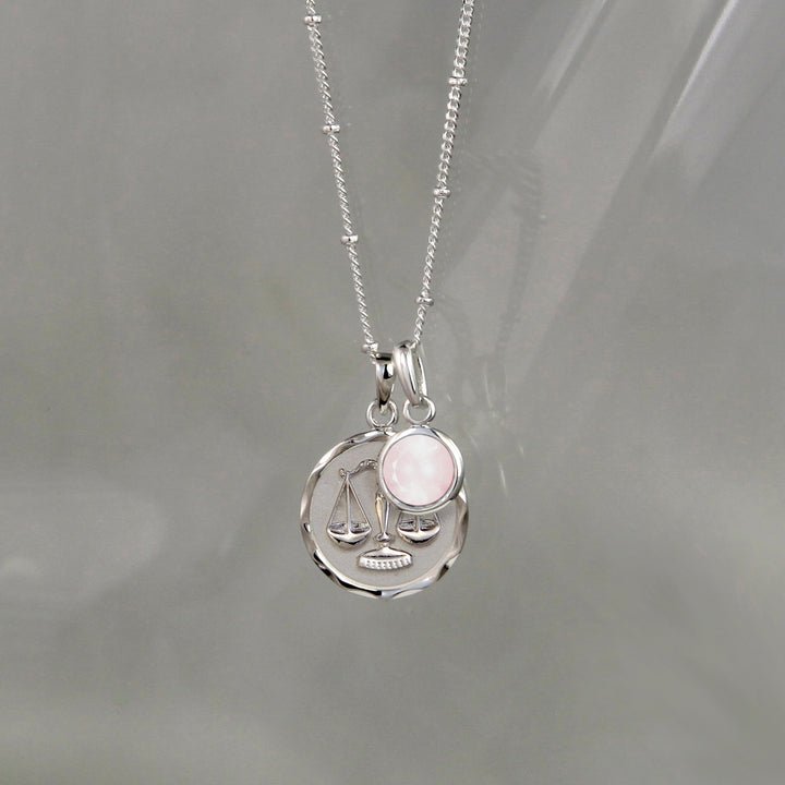 Silver Libra zodiac necklace and rose quartz October birthstone charm on a gray background