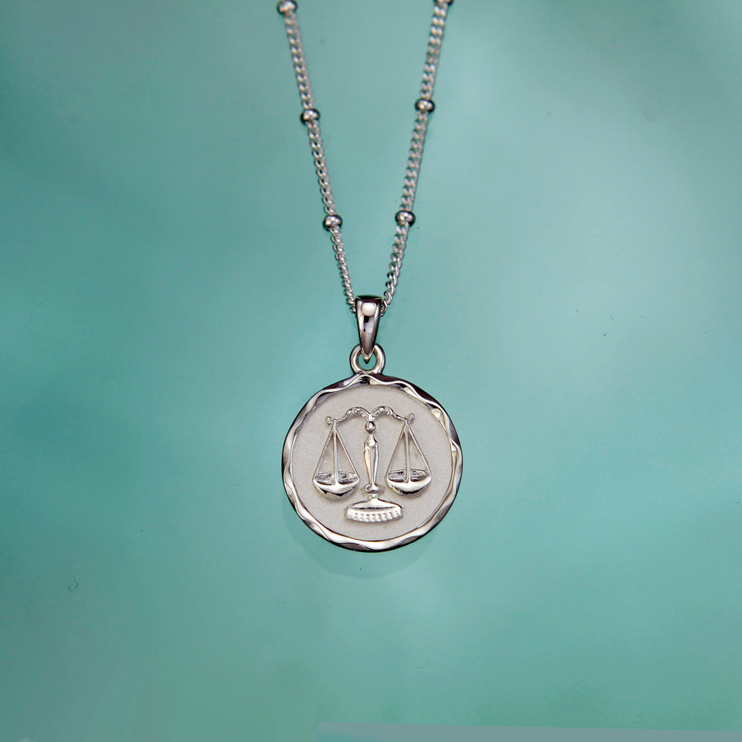 Silver Libra zodiac necklace on an aqua background