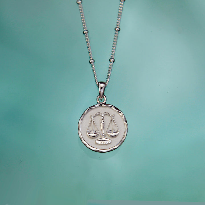 Silver Libra zodiac necklace on an aqua background