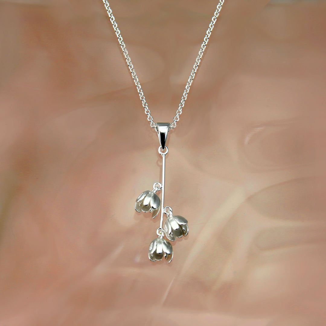 Silver necklace with three pendant flowers on a soft brown background