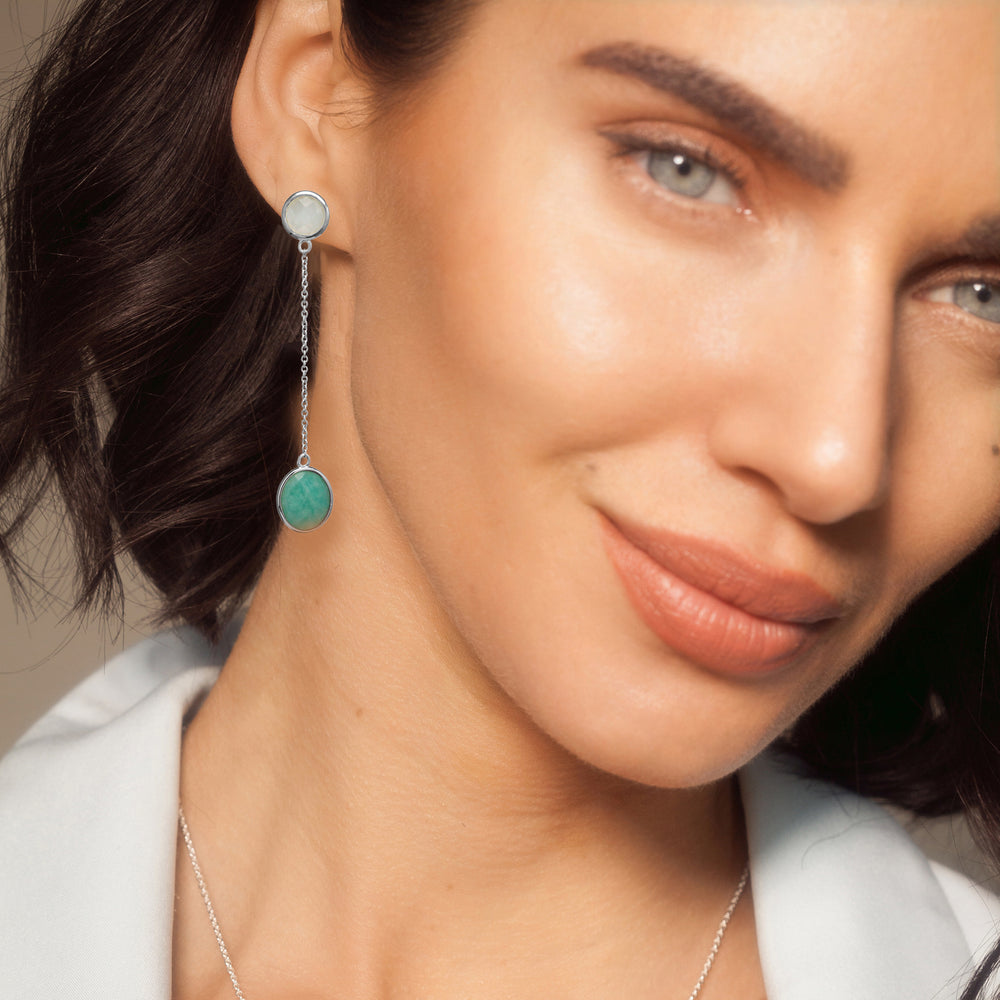 Model wearing silver drop earrings with both a white and green oval gemstones