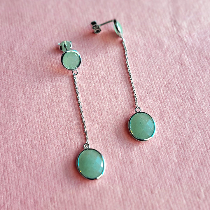 Sterling silver long drop earrings with jade-green aventurine gemstones on a pink background