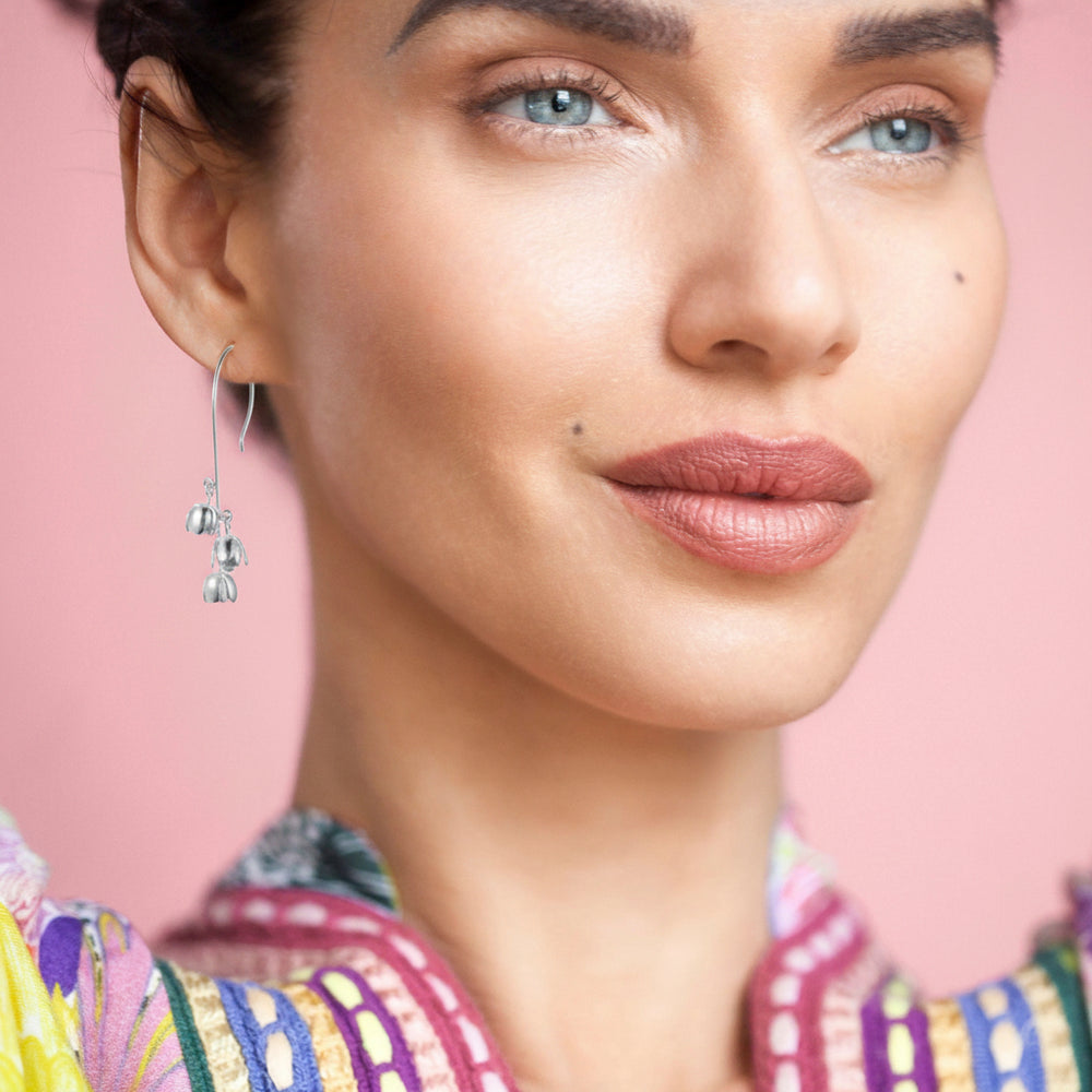 Close-up of a woman wearing silver long drop lily of the valley flower earrings