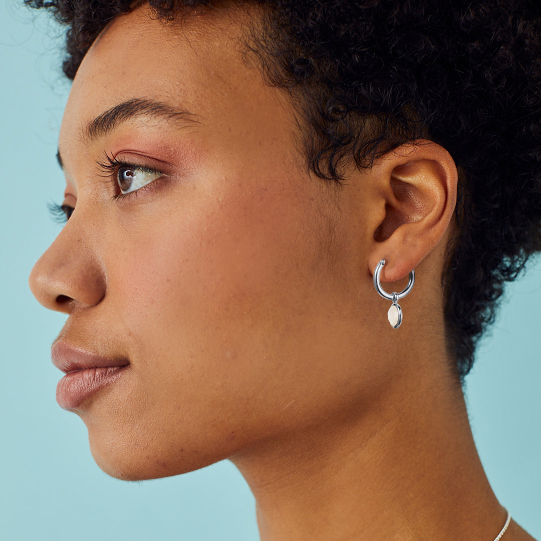 Close-up of a woman wearing a silver hoop earring with moonstones against a light blue background