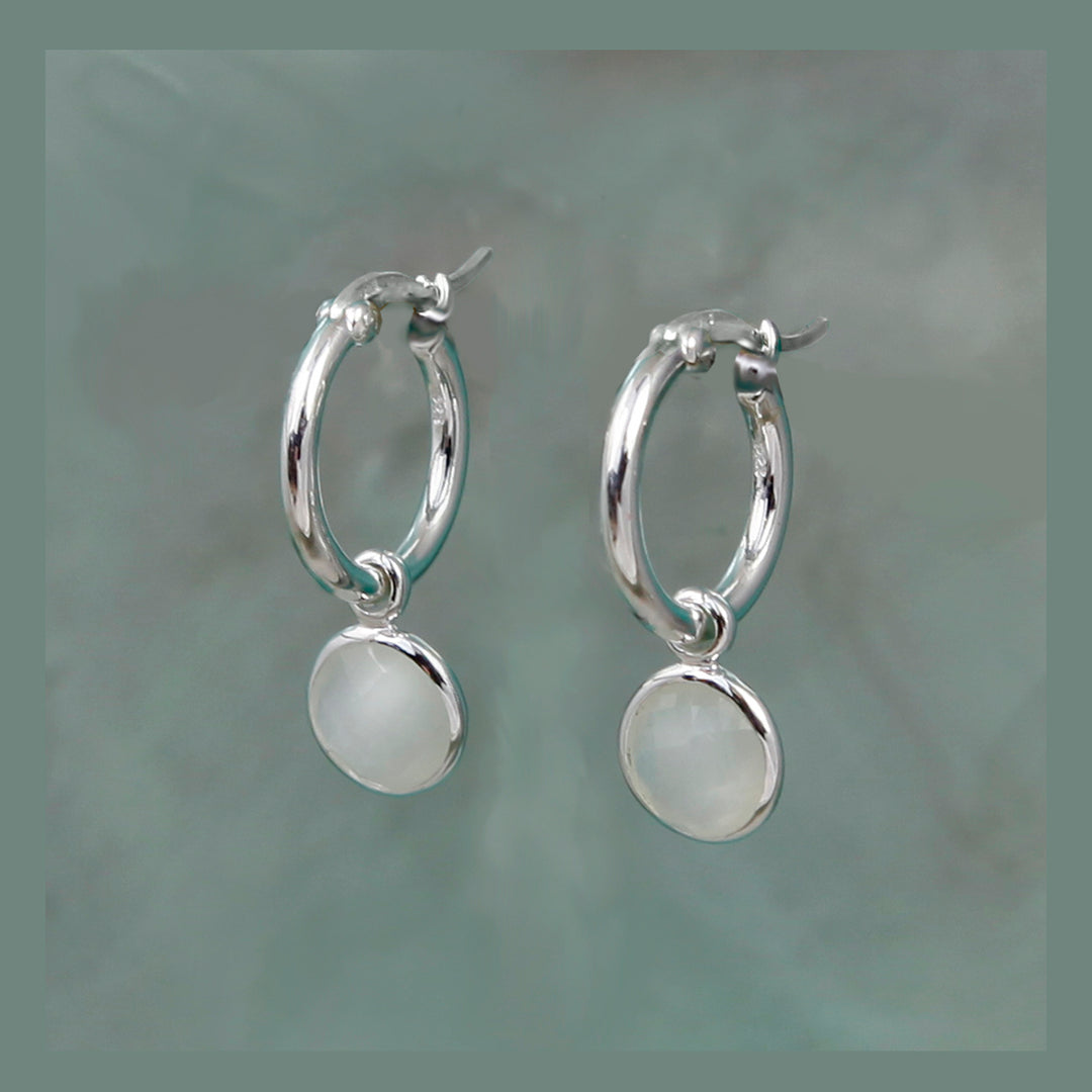 Silver hoop earrings with round moonstone pendants on a gray background