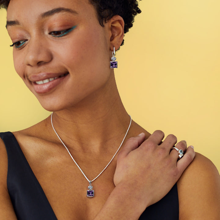 Woman wearing silver earring and necklace set with square amethysts and blue topaz gemstones against a yellow background