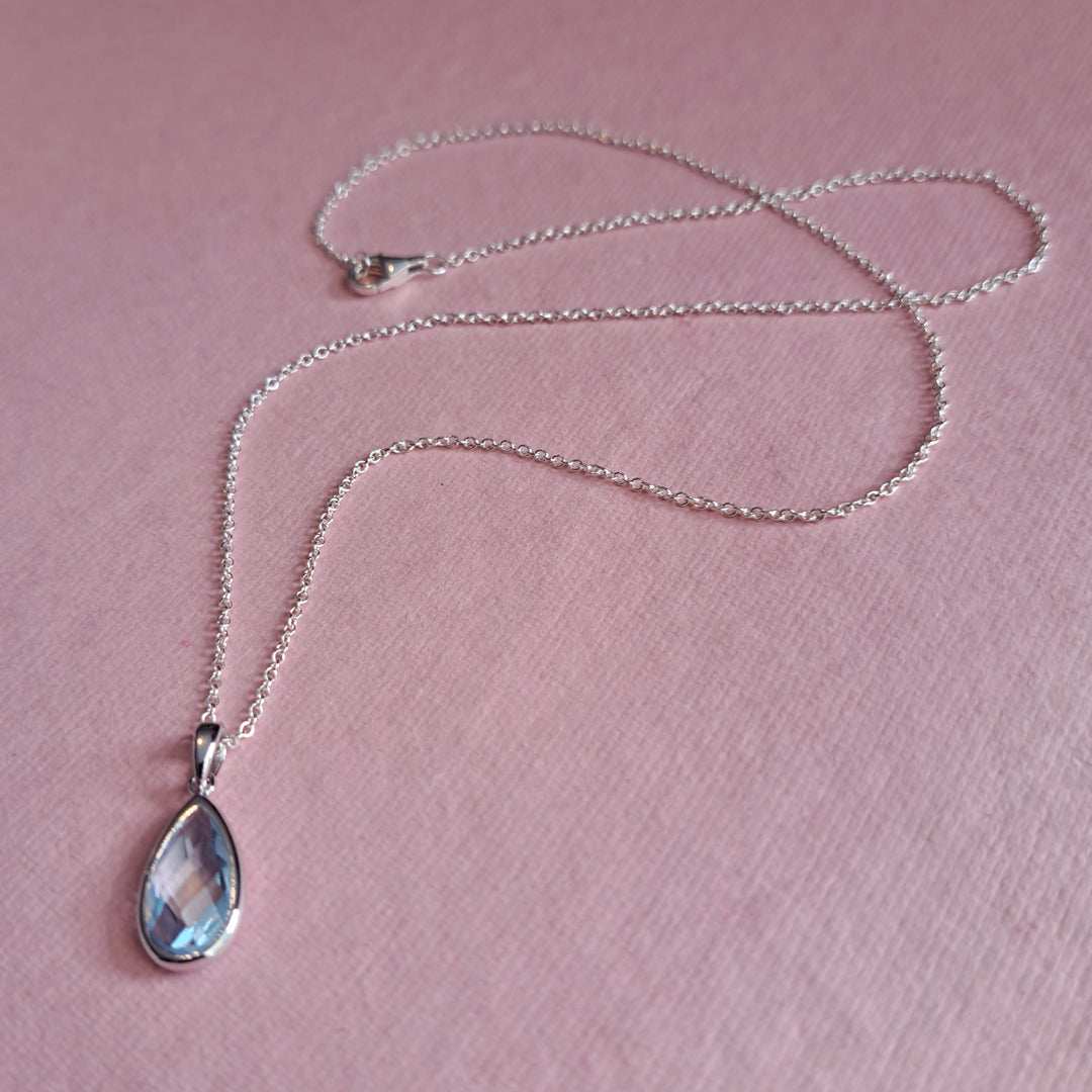 Sterling silver pear drop pendant necklace in blue topaz on a pink background