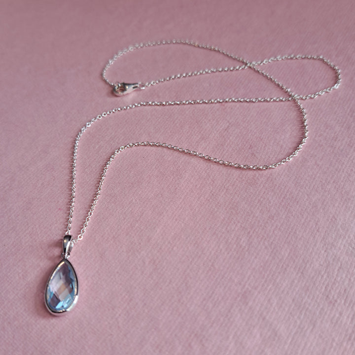 Sterling silver pear drop pendant necklace in blue topaz on a pink background