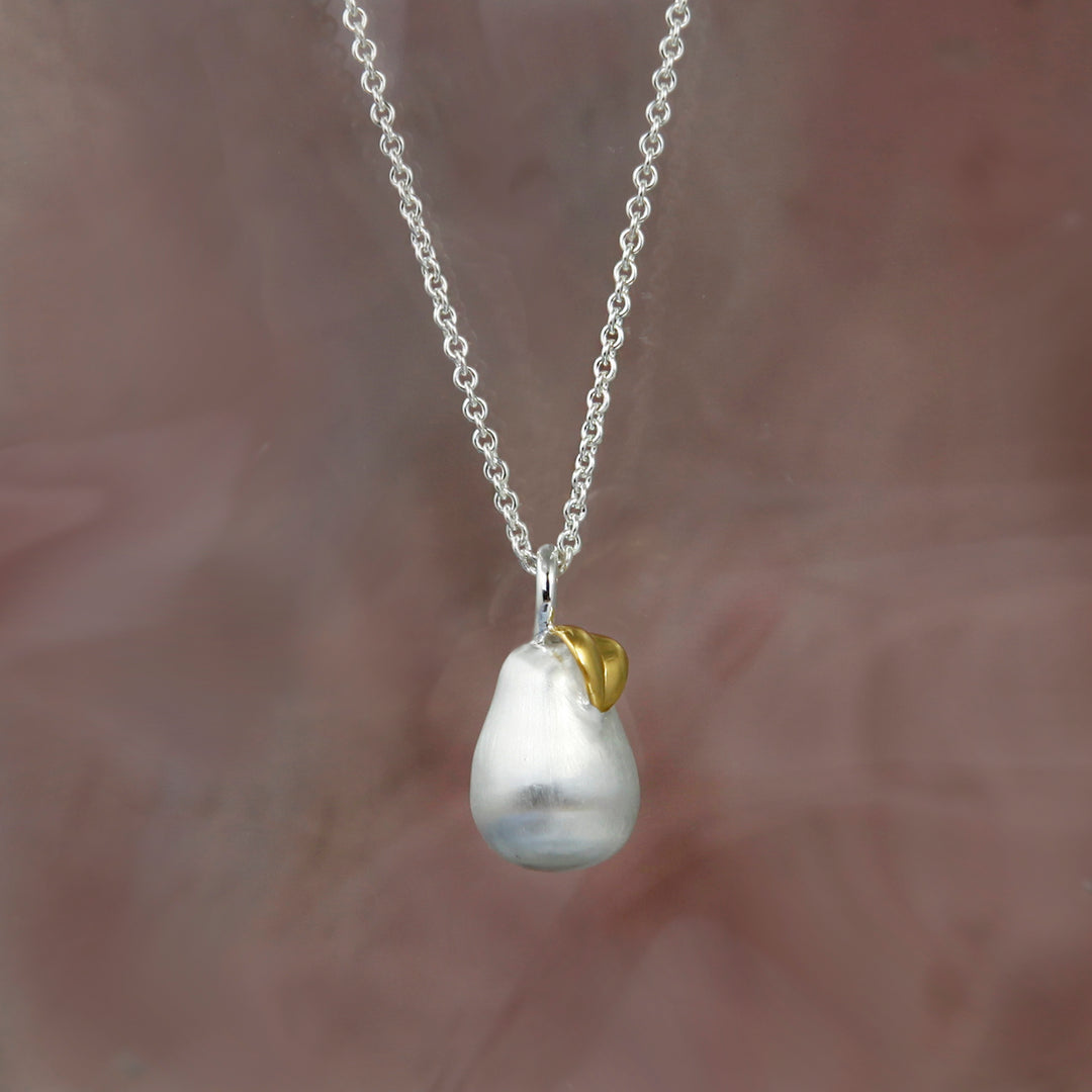Silver pear pendant necklace with a gold leaf on a beige background