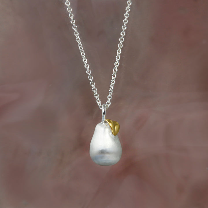 Silver pear pendant necklace with a gold leaf on a beige background