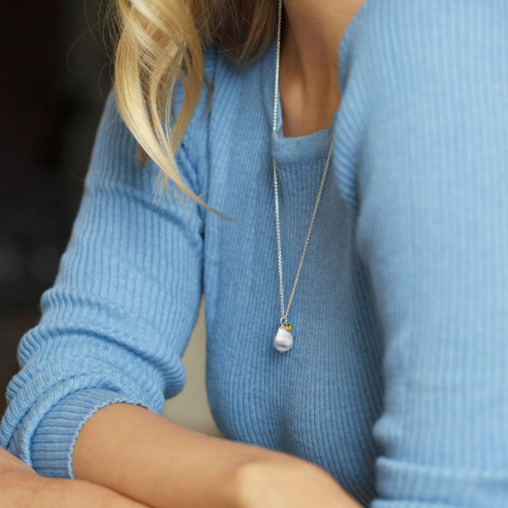 Person wearing silver pear pendant on a blue sweater
