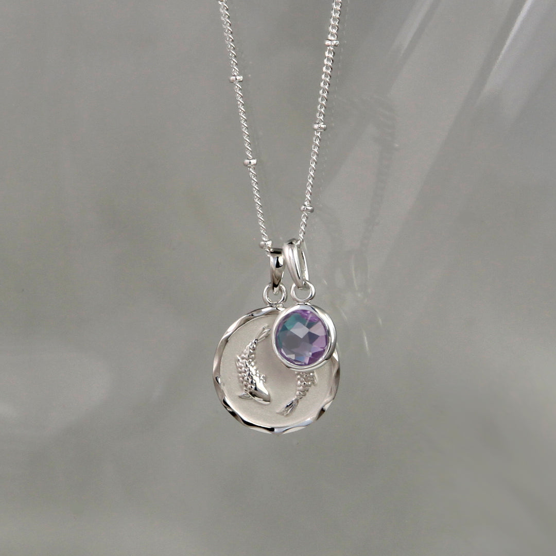 Silver Pisces pendant and amethyst february birthstone charm on a gray background