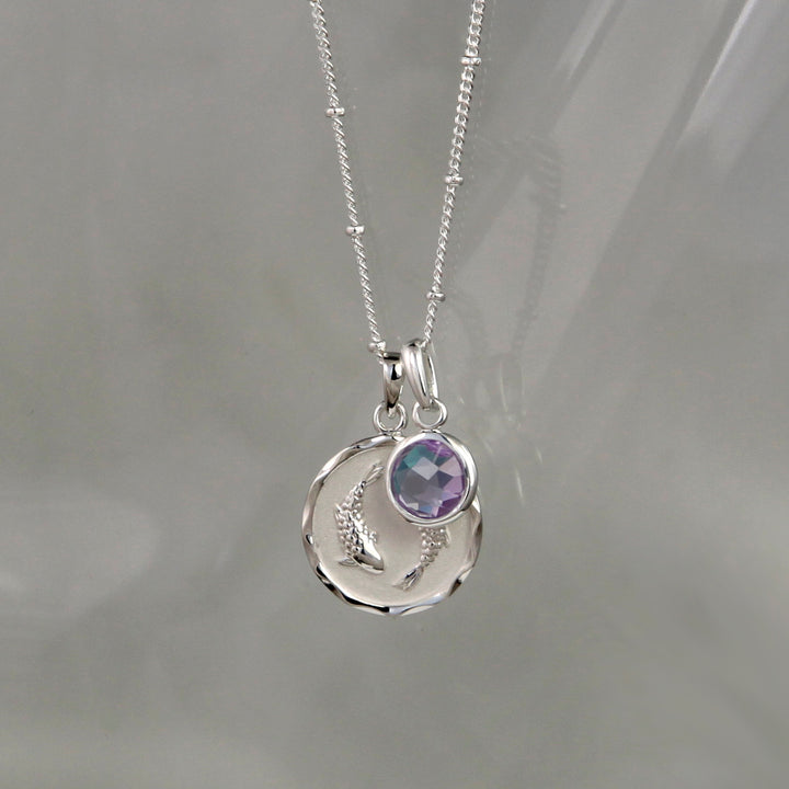 Silver Pisces pendant and amethyst february birthstone charm on a gray background