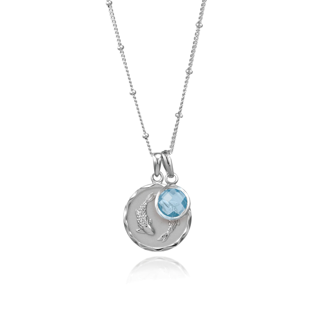 SIlver zodiac pendant and blue topaz gemstone charm on white background