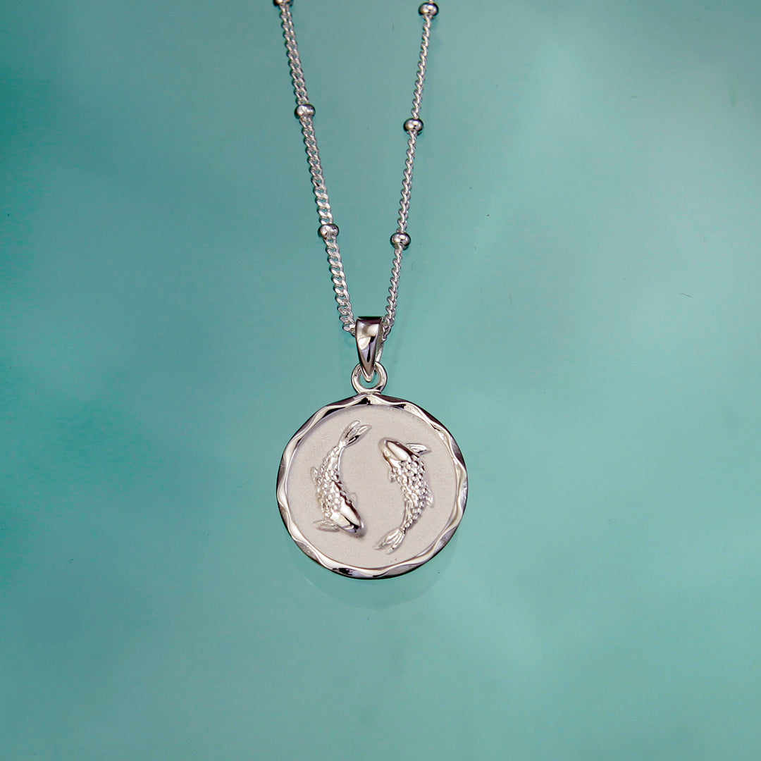 Silver pisces necklace and chain on an aqua background