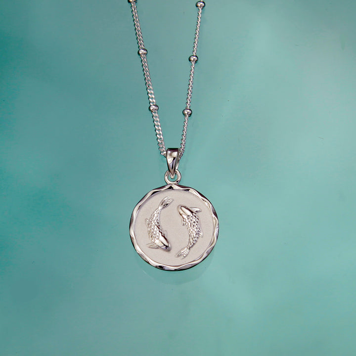 Silver pisces necklace and chain on an aqua background