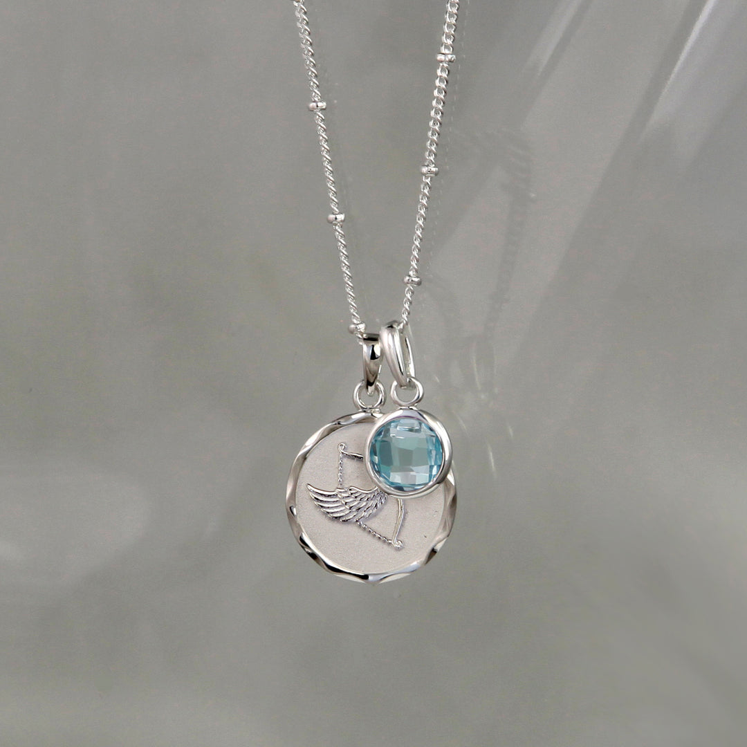 Silver sagittarius zodiac pendant and blue topaz December birthstone charm on a gray background