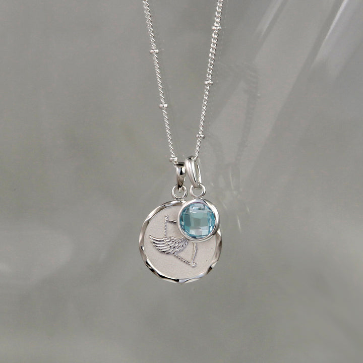 Silver sagittarius zodiac pendant and blue topaz December birthstone charm on a gray background