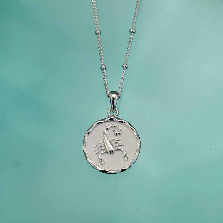 Silver zodiac star sign necklace on an aqua background