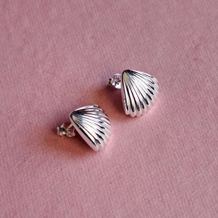 Sterling silver seashell stud earrings on a pink background
