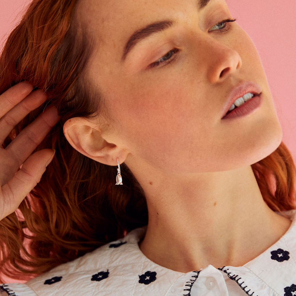 Close-up of a woman wearing a  silver bluebell earring with a pink background