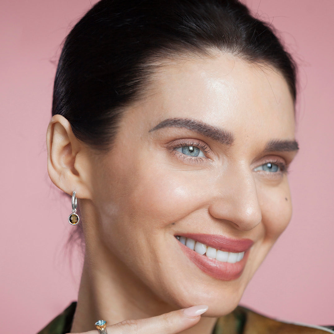Close-up of woman wearing silver hoop earrings with cognac quartz charms