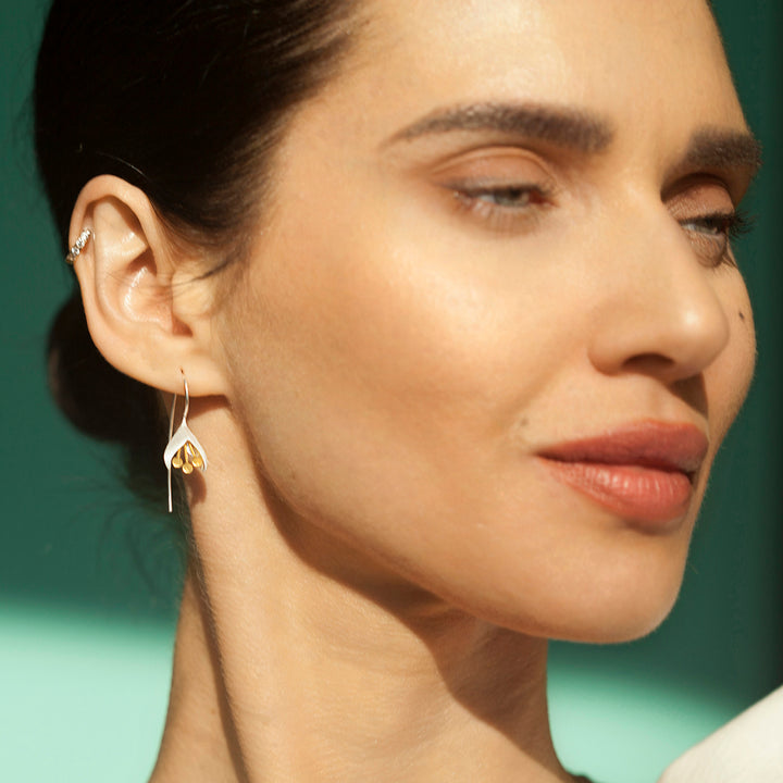 Close-up of a woman wearing silver and gold snowdrop earrings with a green background