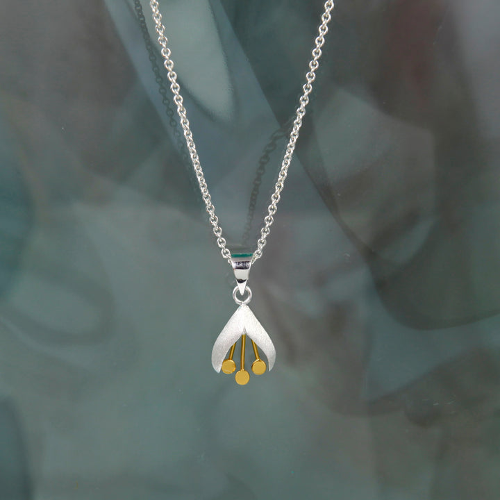 Silver and gold snowdrop necklace and chain on a dark reflective surface