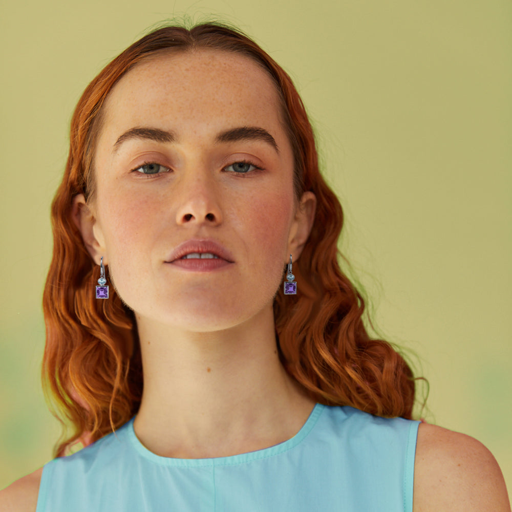Woman with red hair wearing purple and blue earrings against a green background