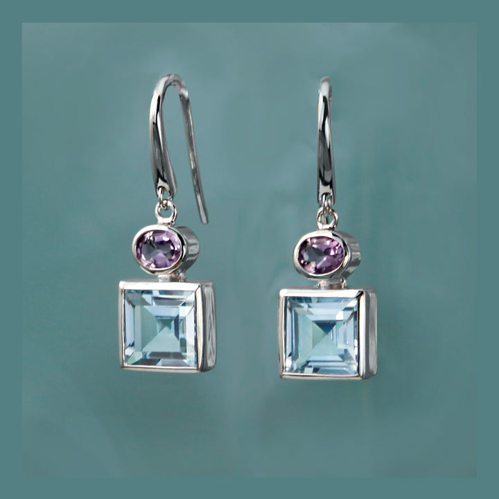 Square silver earrings with blue and purple gemstones on a gray background