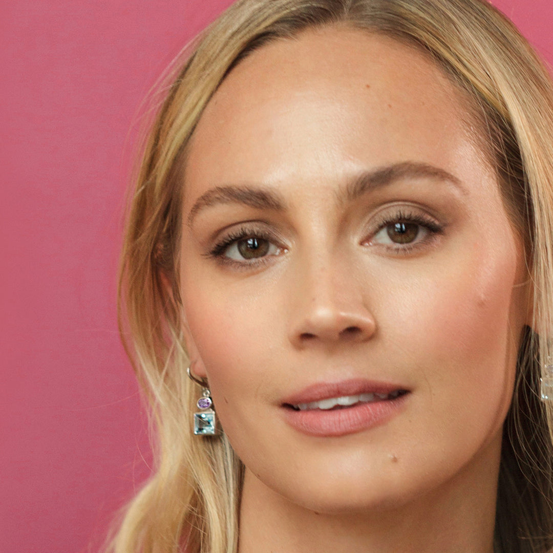Close-up of a blond model wearing silver ,blue topaz and amethyst gemstones against a pink background