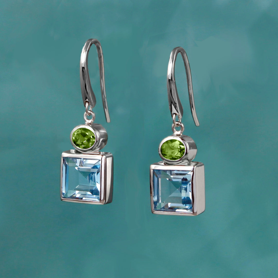 Square silver earrings with blue topaz and peridot gemstones on a teal background