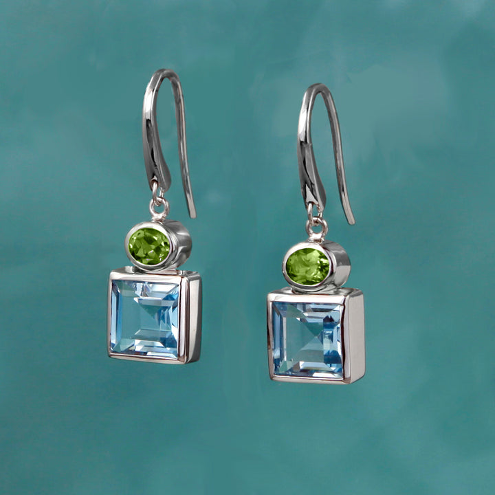 Square silver earrings with blue topaz and peridot gemstones on a teal background