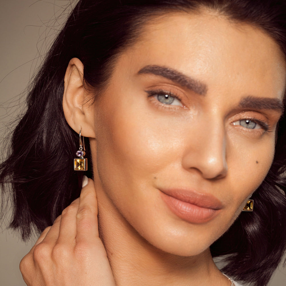 Close-up of a woman wearing silver earrings with citrine and amethyst gemstones