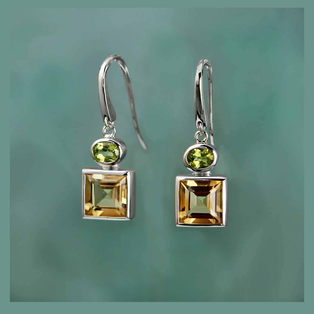 Pair of silver earrings with square-cut citrine and peridot gemstones on a green background