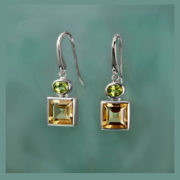 Pair of silver earrings with square-cut citrine and peridot gemstones on a green background