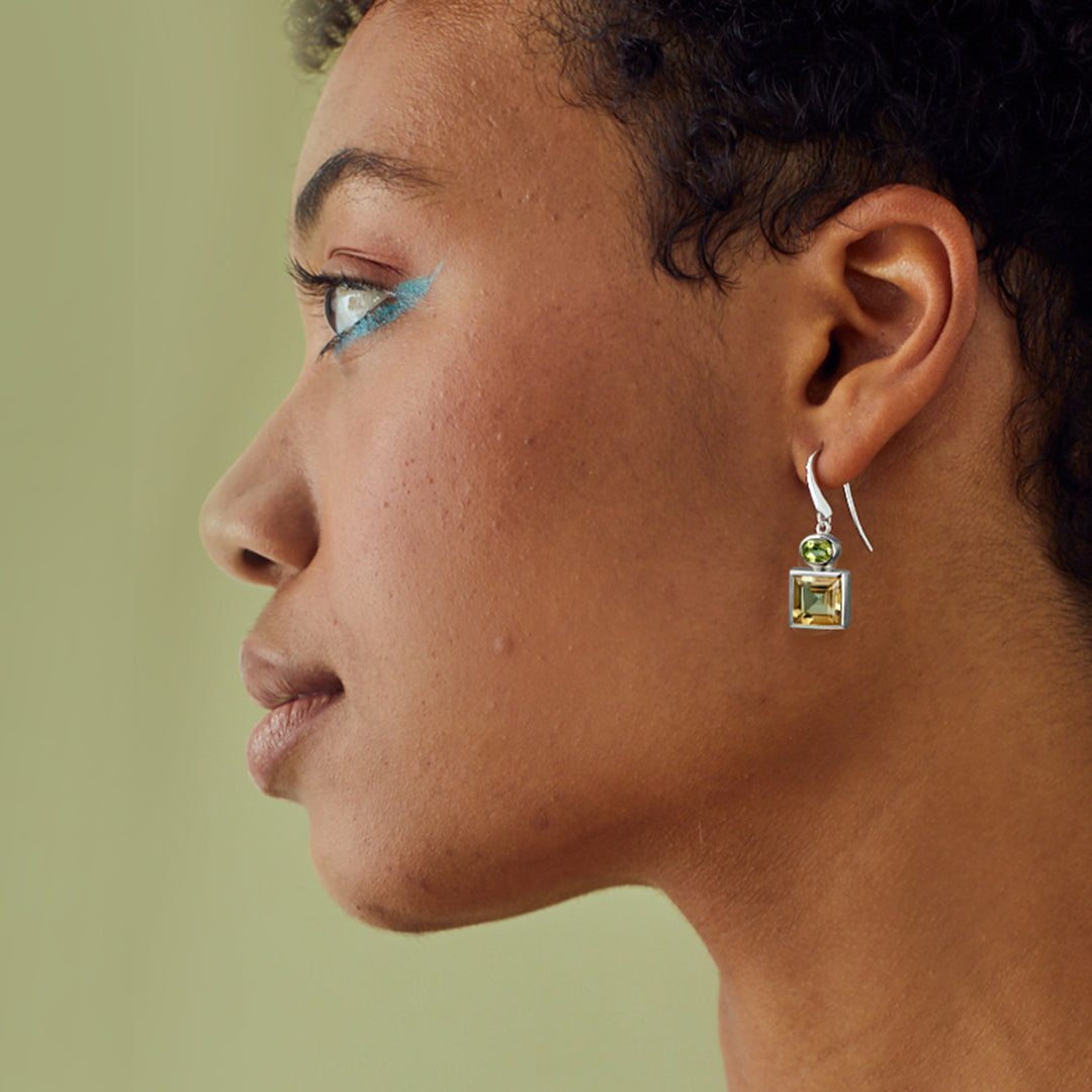 Close-up of a person wearing square silver earrings set with yellow citrine and green peridot gemstones