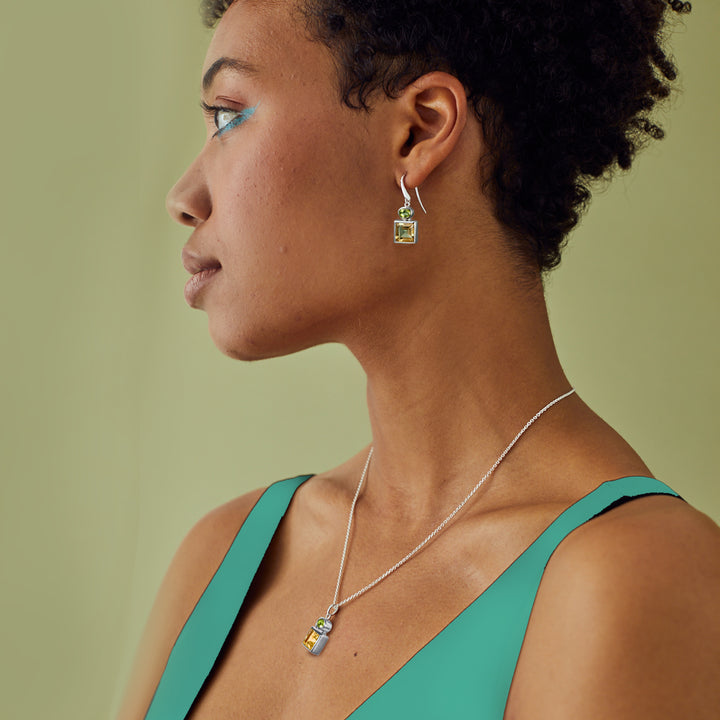 Woman wearing a silver necklace and matching earrings set with square citrine and oval peridot gemstones