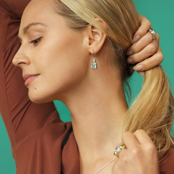 Woman holding back her hair wearing silver earrings with blue topaz and peridot gemstones