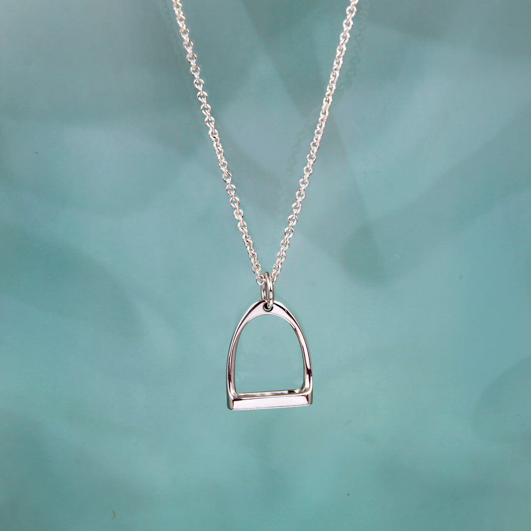 Silver equestrian stirrup pendant on a chain against a teal background