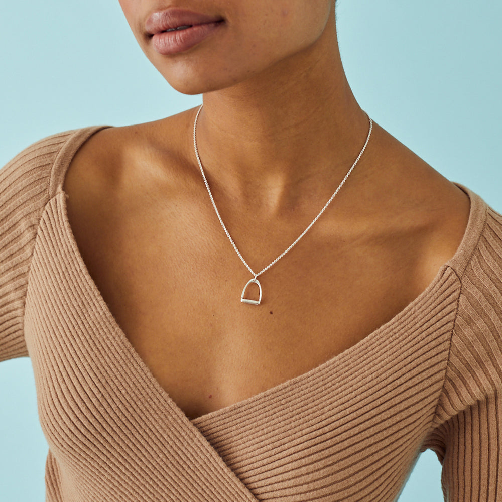 Closes up of a  model wearing a silver stirrup necklace with a beige top