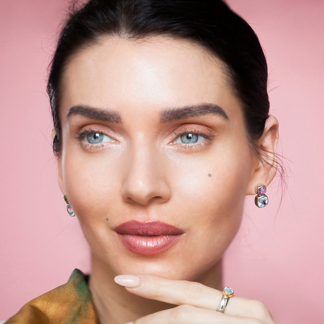 Close-up of a woman wearing silver stud earrings set with amethyst and blue topaz gemstones