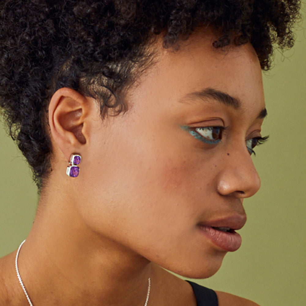 Close-up of model wearing silver earrings with amethyst gemstones